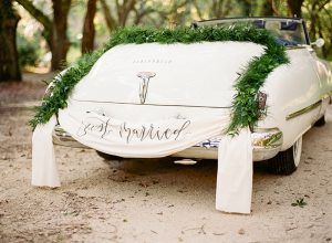 A white car decorated with greenery and a just married sign.