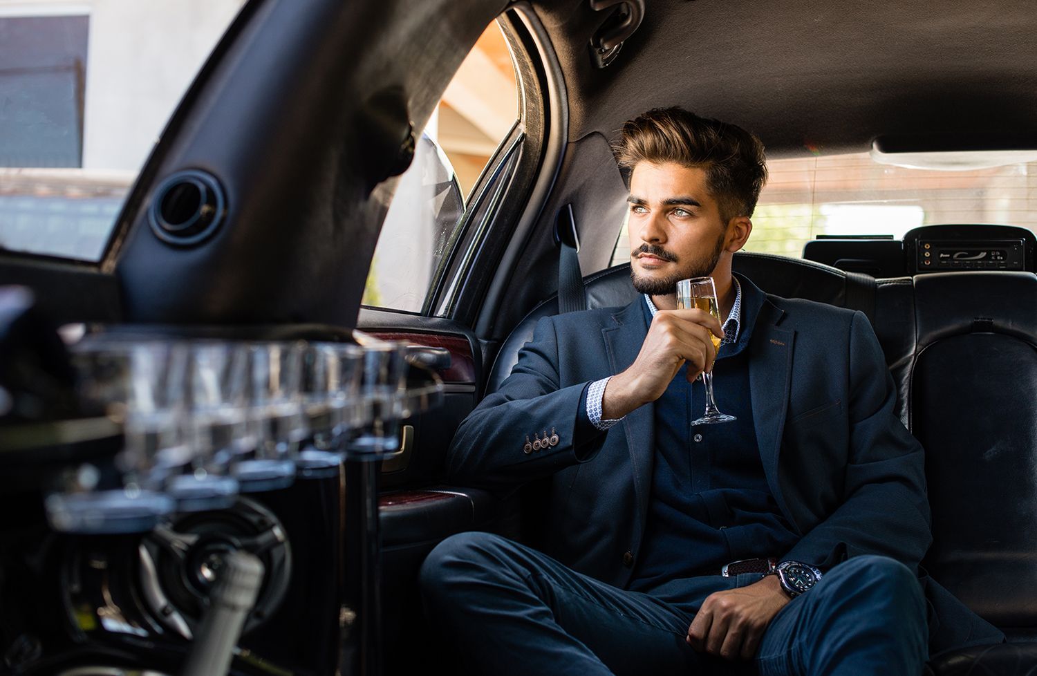 A man is sitting in the back seat of a limousine holding a glass of champagne.
