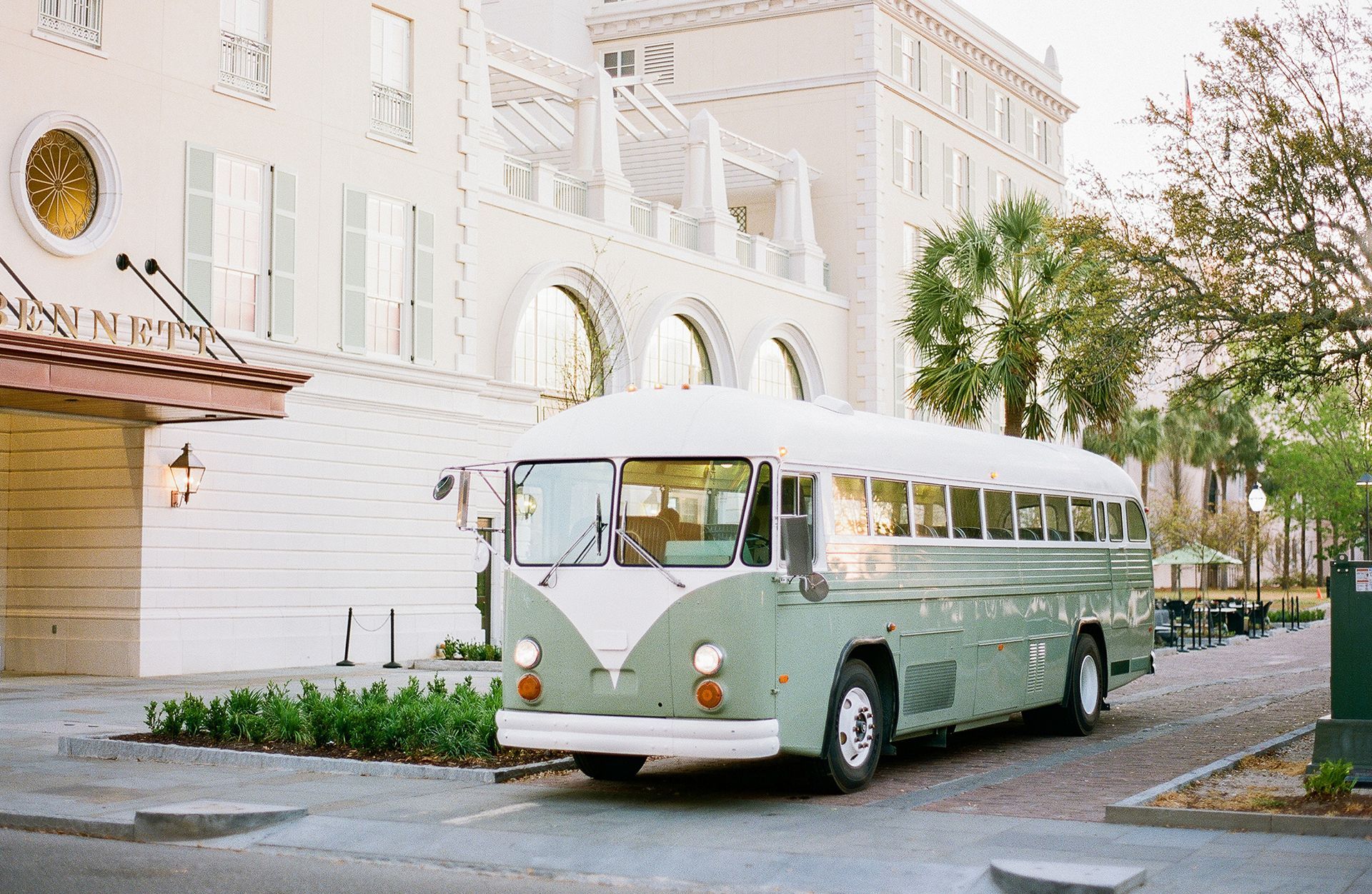 A green and white bus is parked in front of a white building.