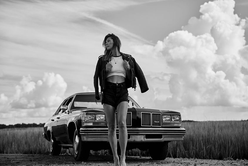 A woman is standing next to a car in a field.