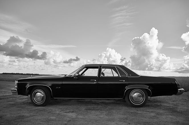 A black and white photo of an old car parked on the side of the road.