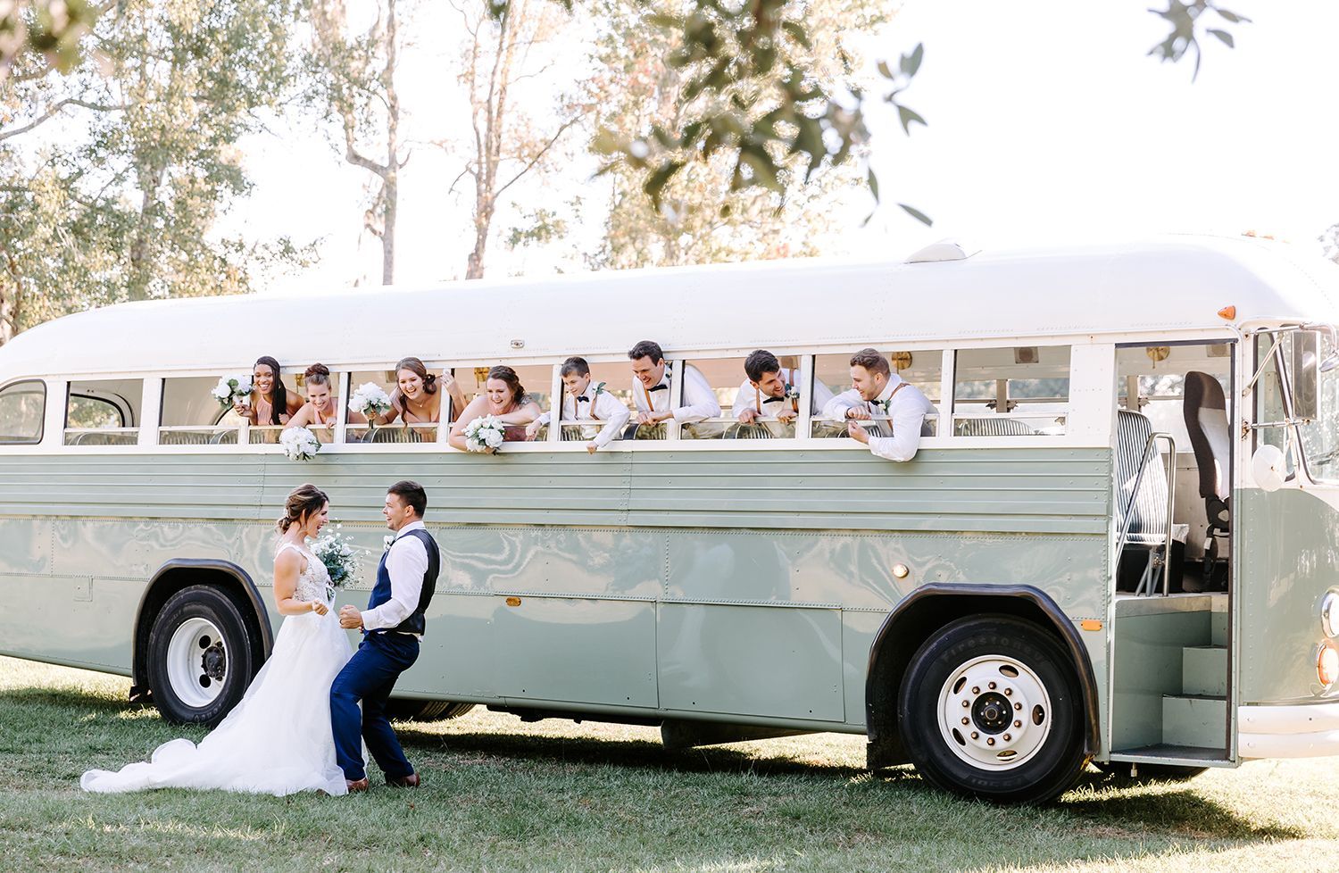 A bride and groom are standing next to a wedding bus.