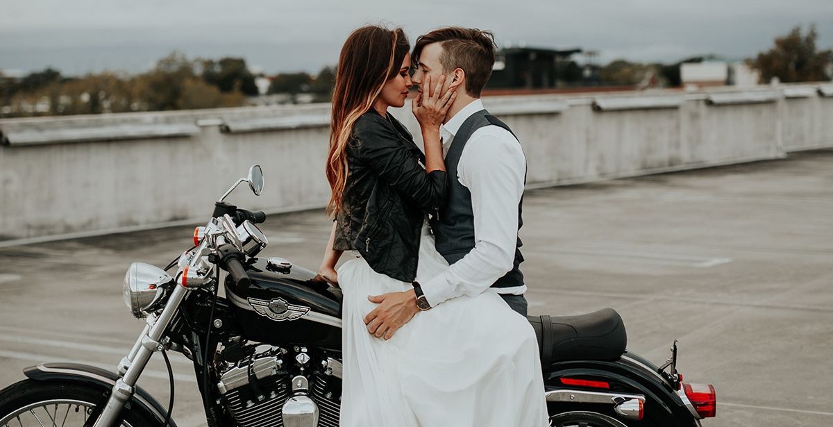 A bride and groom are kissing on a motorcycle.