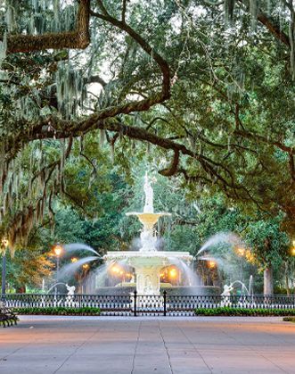 A fountain in a park surrounded by trees and spanish moss.