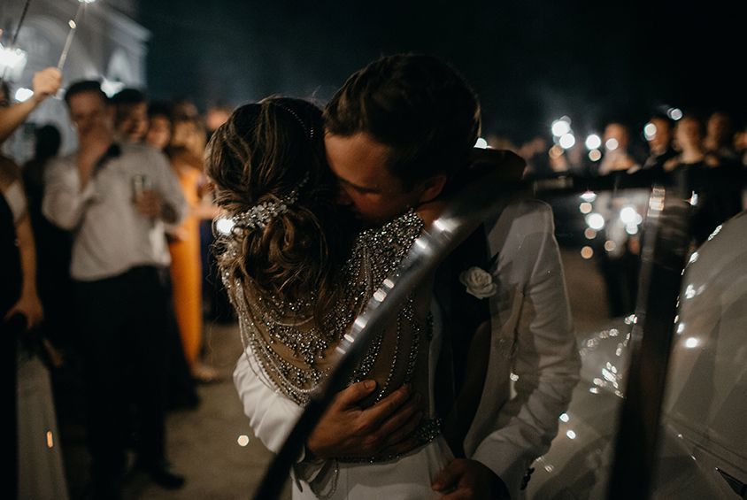 A bride and groom are kissing while holding sparklers at their wedding reception.