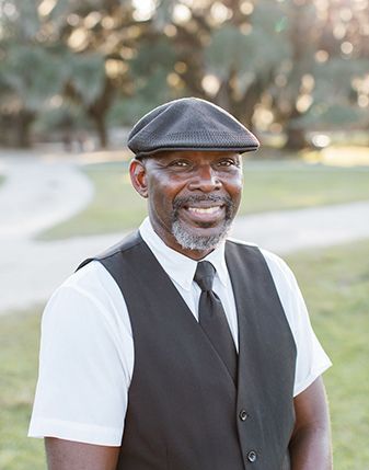 A man wearing a hat and vest is smiling for the camera.