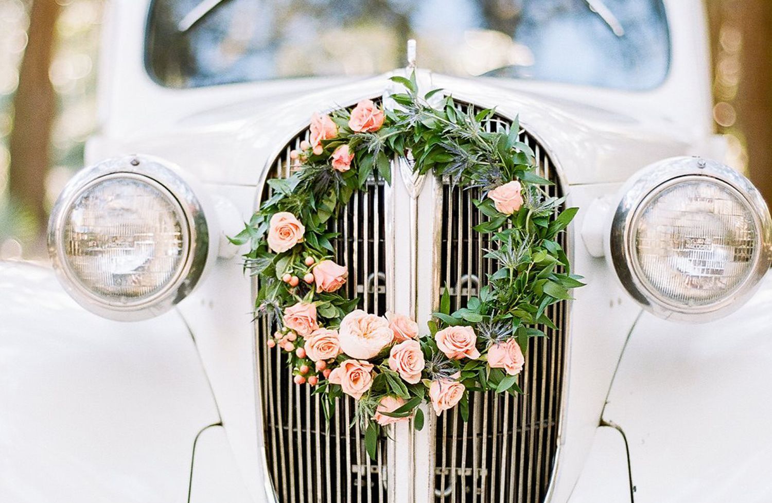 A white car with a wreath of flowers on the grille.