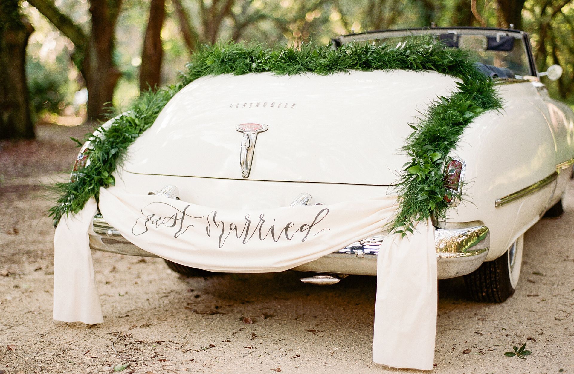 A white car decorated with greenery and a sign that says `` just married ''.