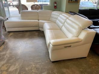 A white leather sectional couch is sitting on a concrete floor in a living room.