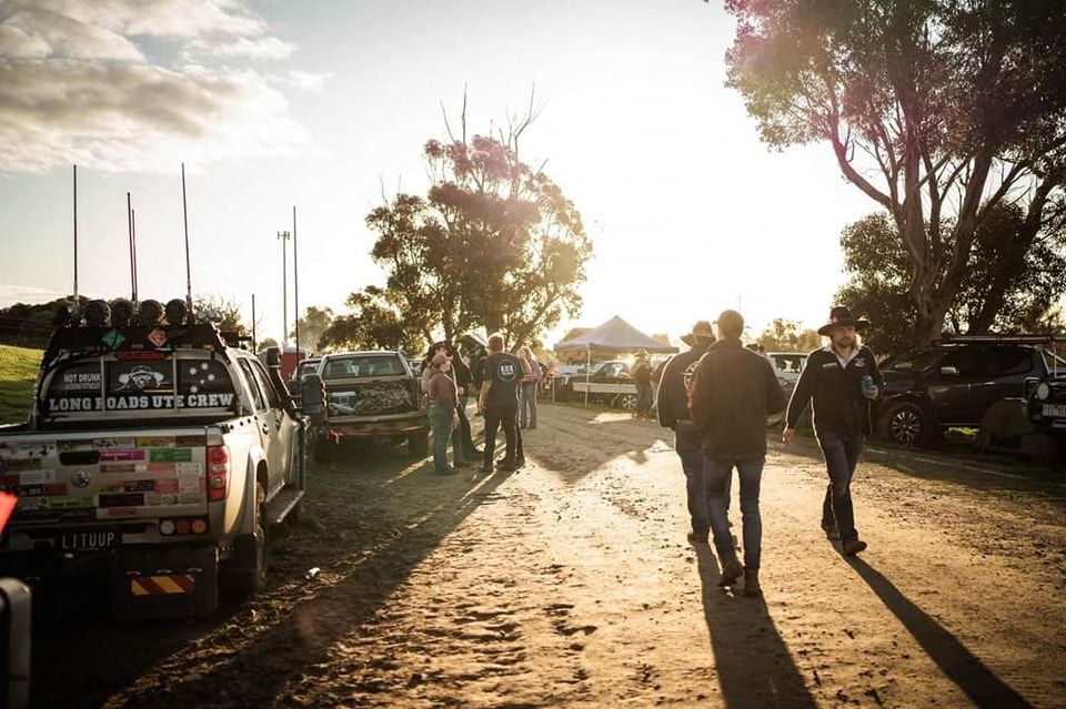 A group of people walking down a dirt road with a truck that says ultimate on the back