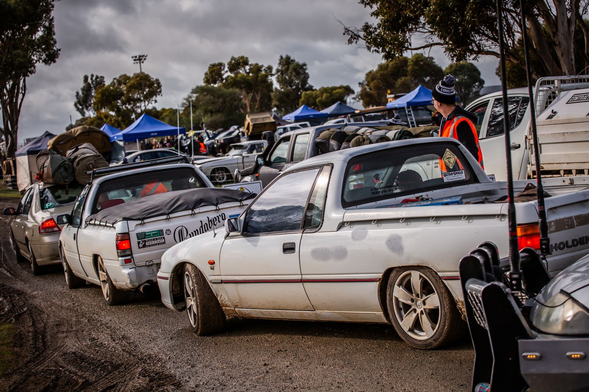 A row of white pickup trucks are parked on a gravel road