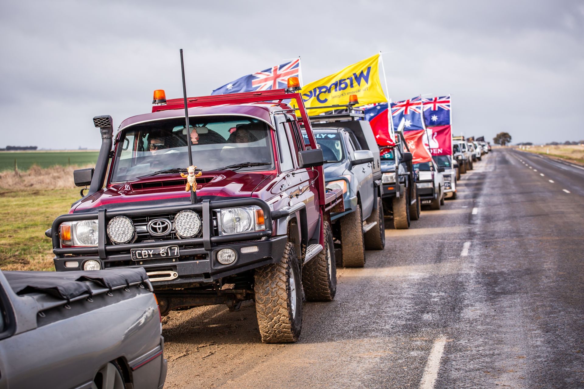A row of trucks are lined up on the side of a road with a yellow flag that says nsw on it