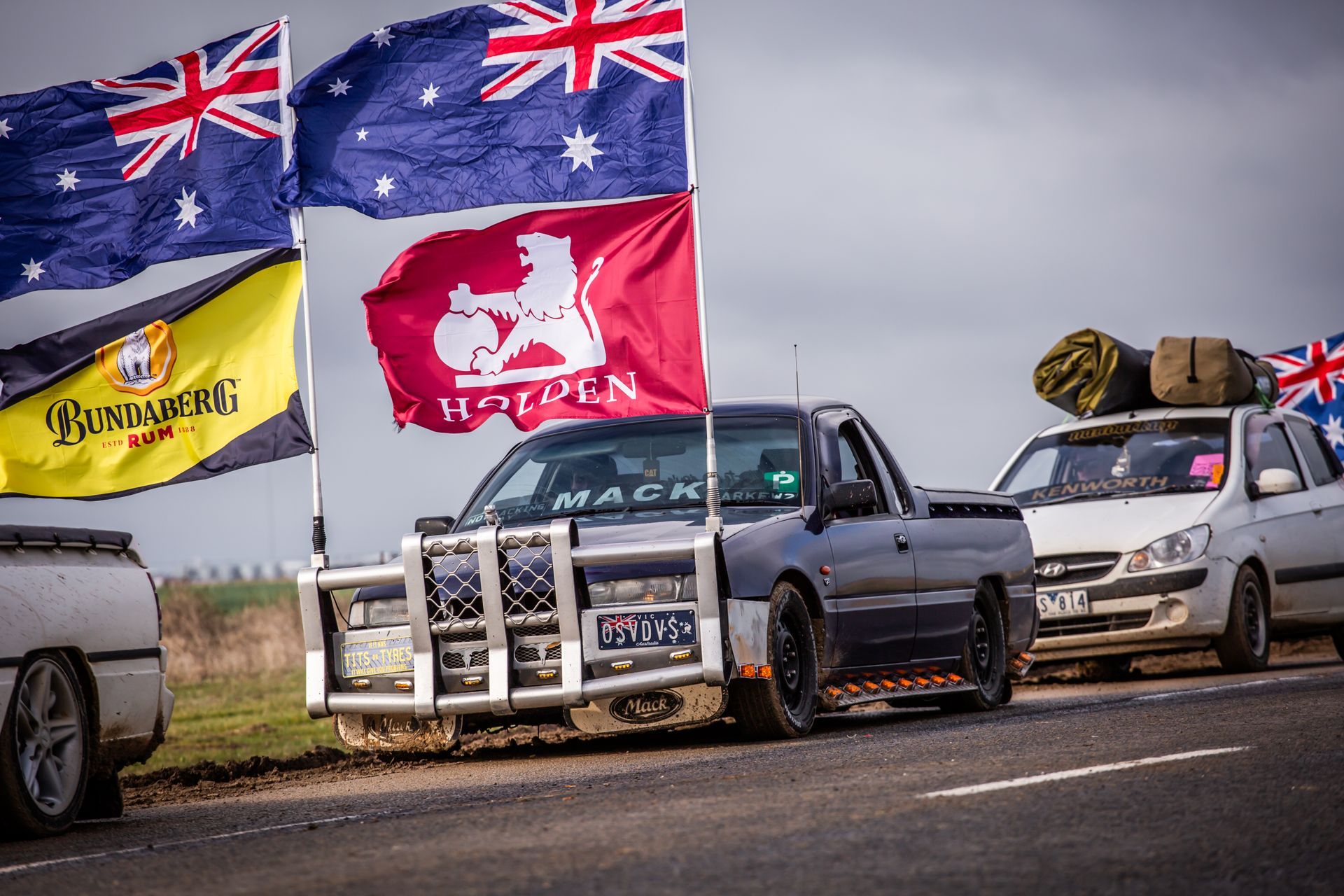A few cars are parked on the side of the road with flags flying in the background