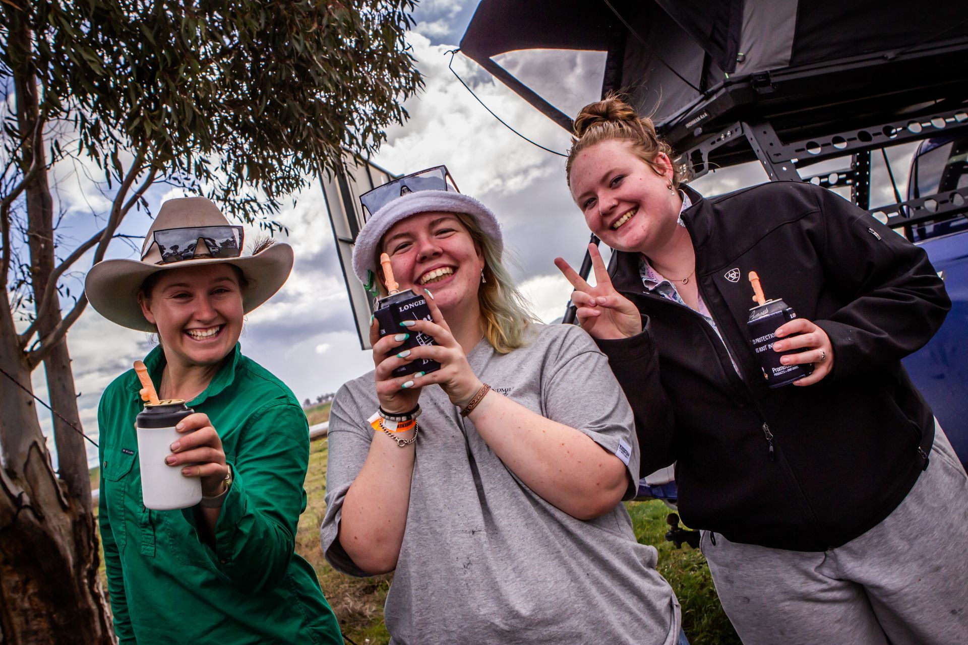 Three women are posing for a picture and one is holding a cell phone