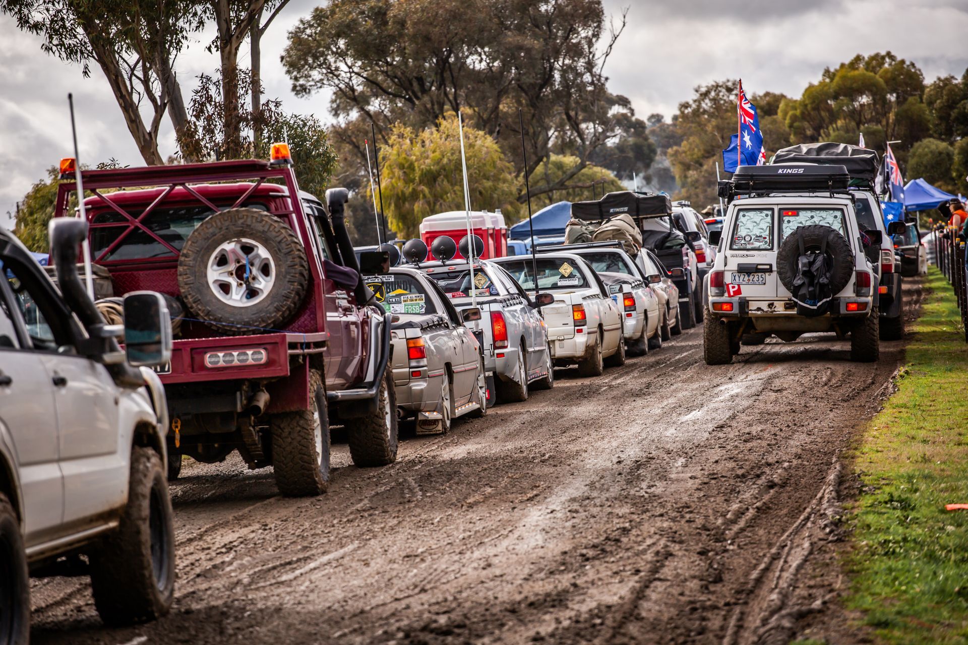 A row of cars are lined up on a muddy road