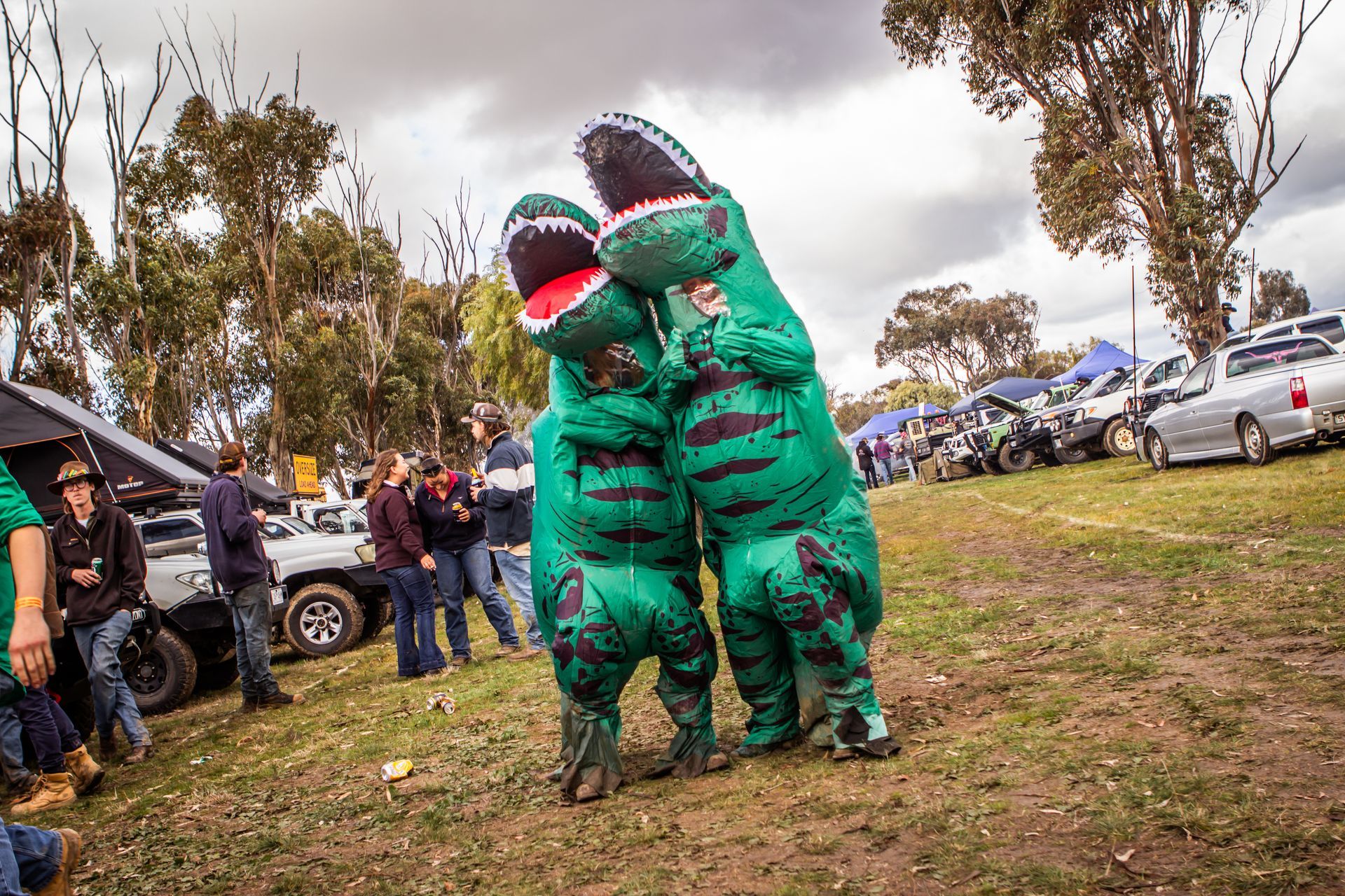 Two people dressed in green dinosaur costumes are hugging each other