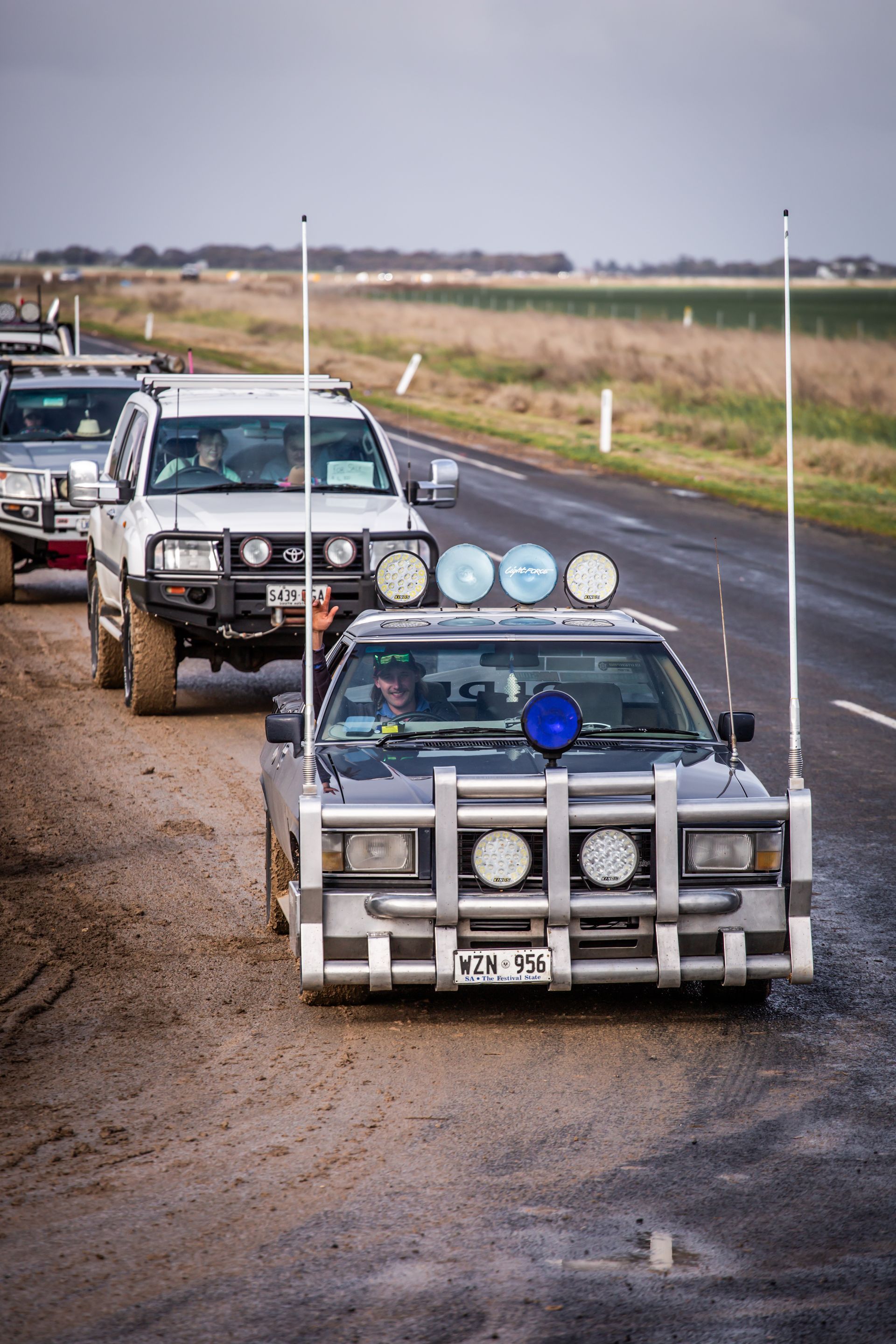 A row of off road vehicles are driving down a dirt road