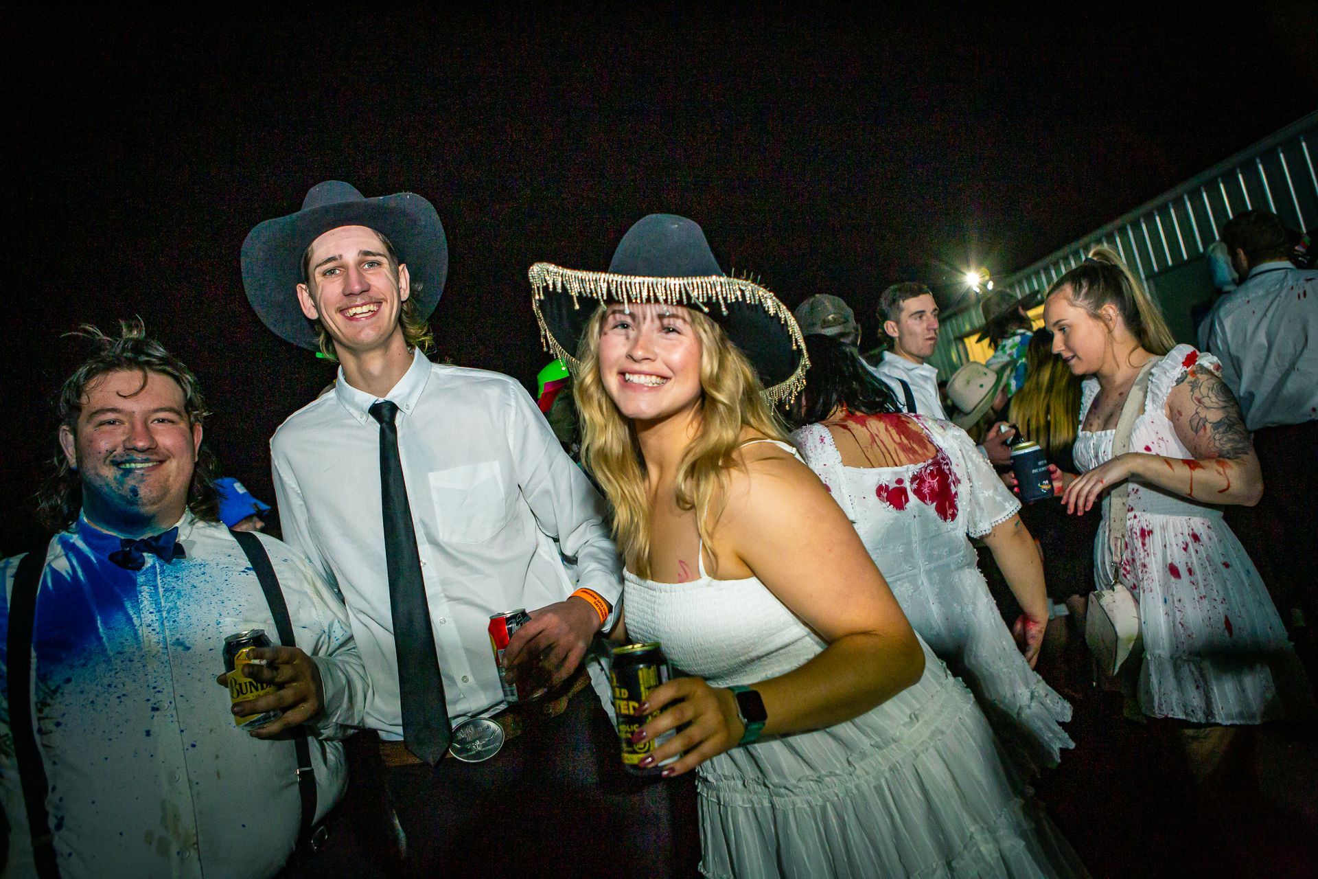 A woman in a white dress and cowboy hat stands in a crowd of people