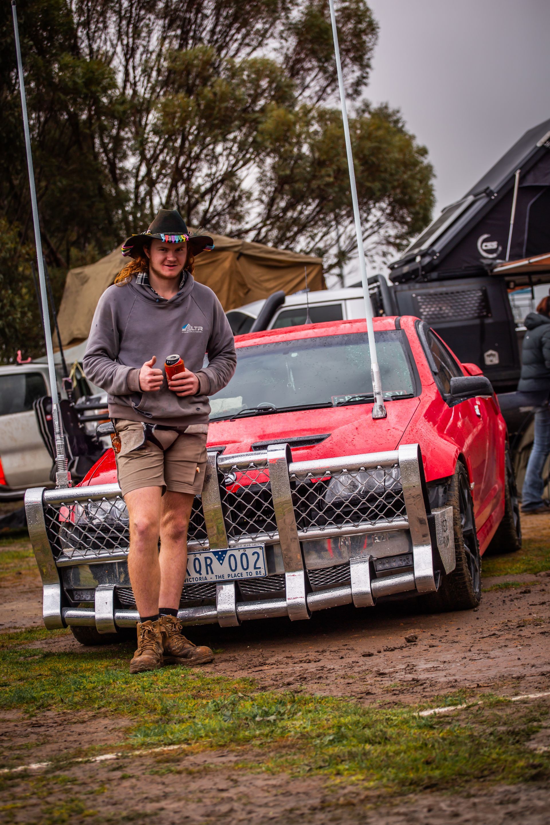 A man in a cowboy hat is standing in front of a red car with a license plate that says tfn-sur