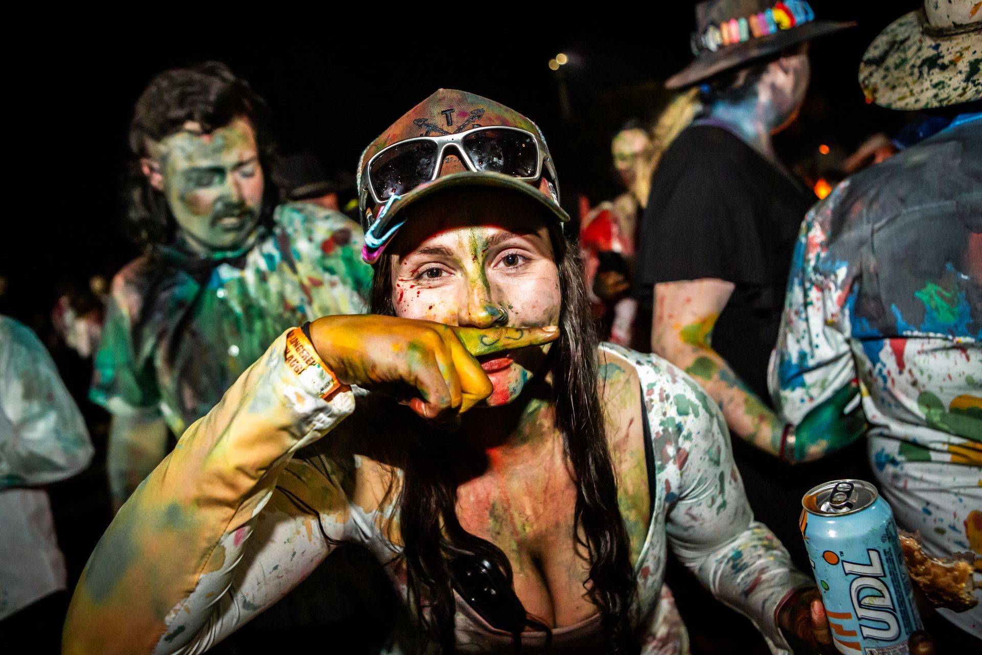 A woman covered in paint is holding a can of beer