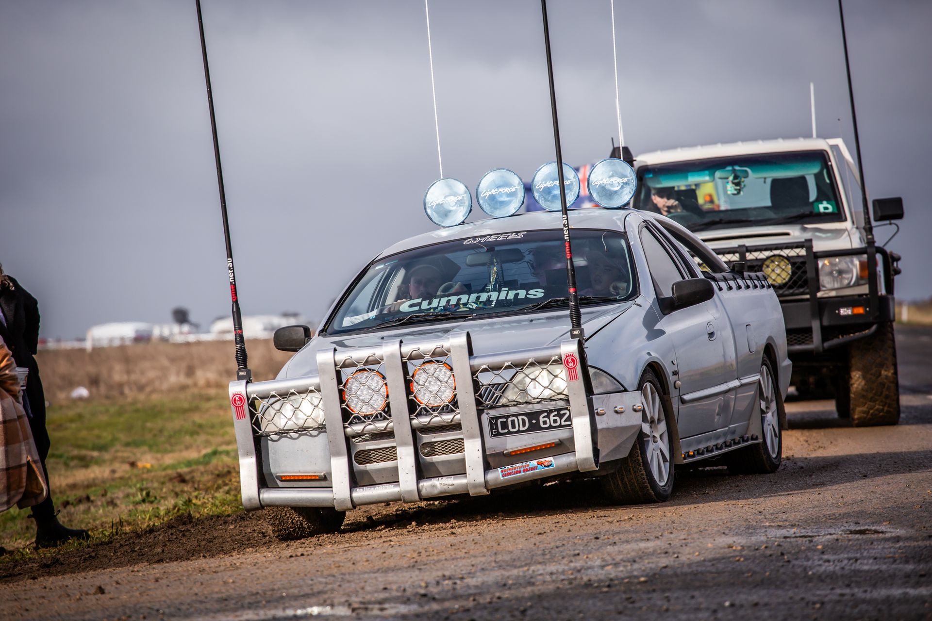 A silver car is parked on the side of the road next to a white truck