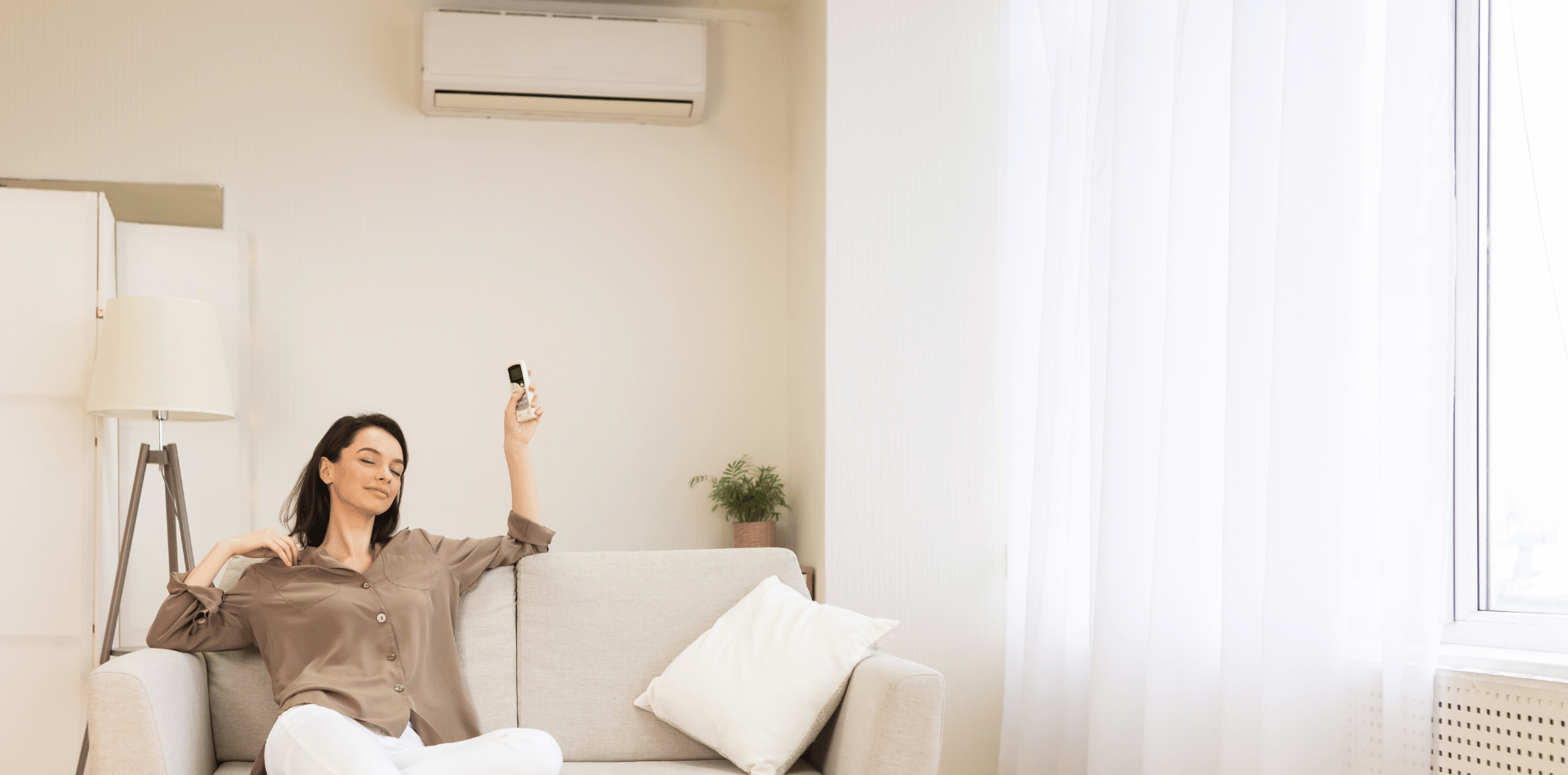 A woman is sitting on a couch in a living room holding a remote control.