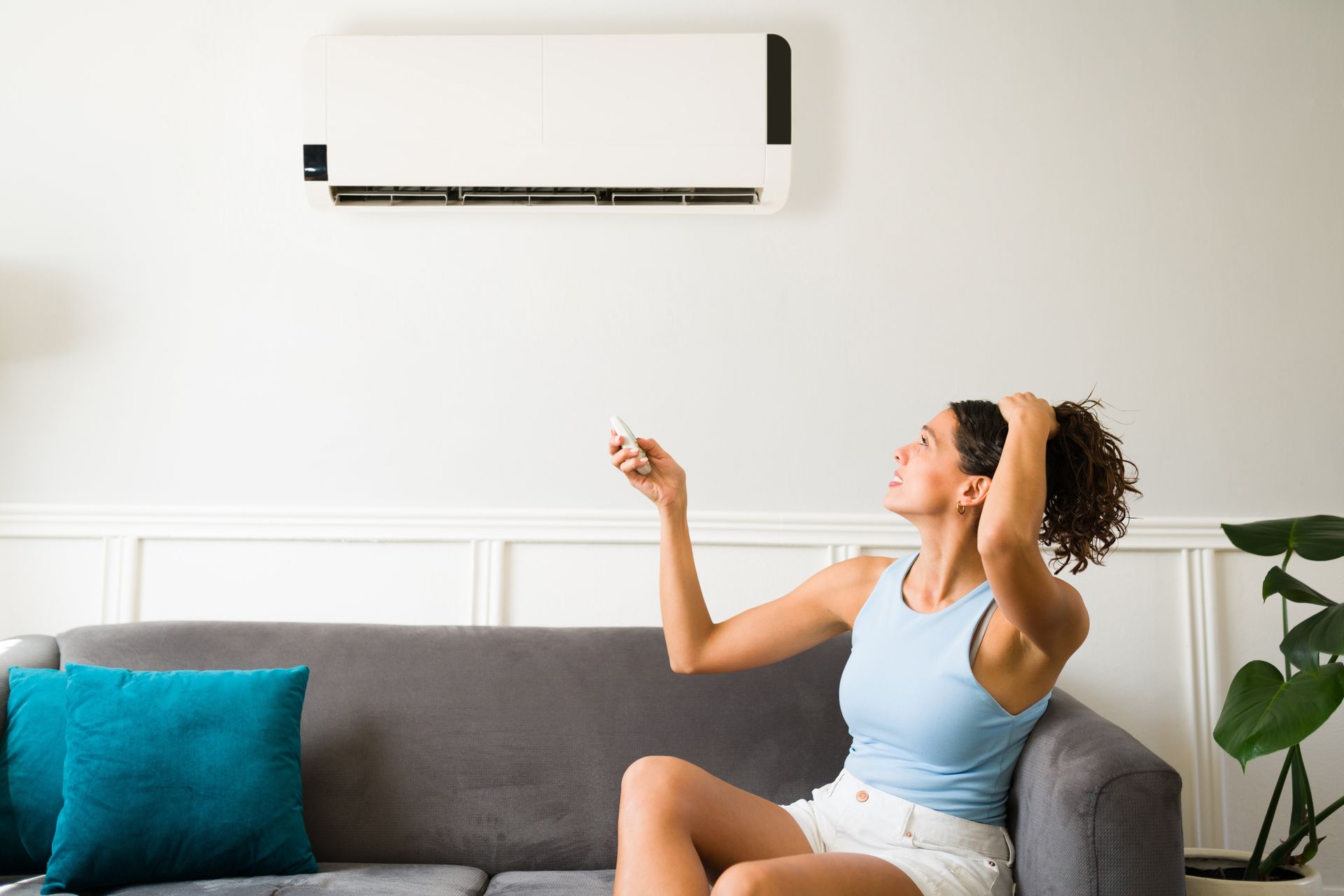 A woman is sitting on a couch in front of an air conditioner.