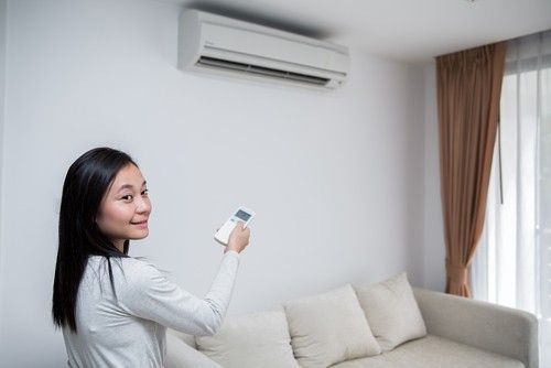 A woman is sitting on a couch in a living room holding a remote control.