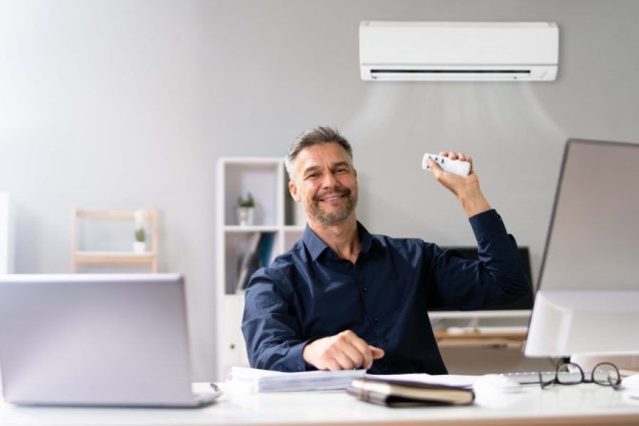 A man is sitting at a desk in an office holding a remote control.
