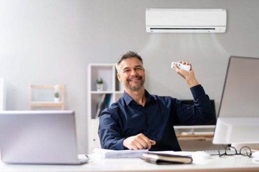 A man is sitting at a desk in an office holding a remote control.