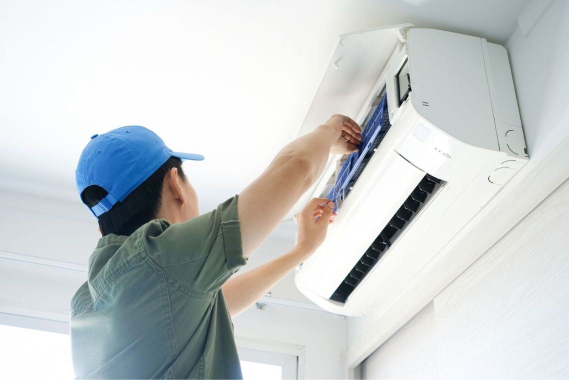 A man in a blue hat is cleaning an air conditioner.