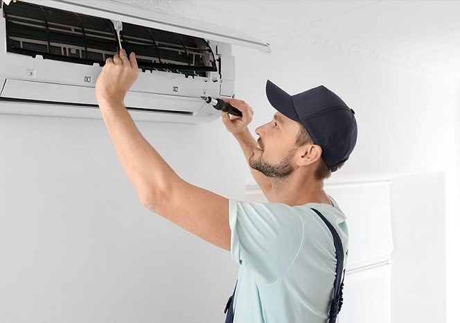 A man is fixing an air conditioner with a screwdriver.