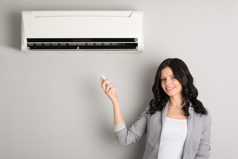 A woman is holding a remote control in front of an air conditioner.