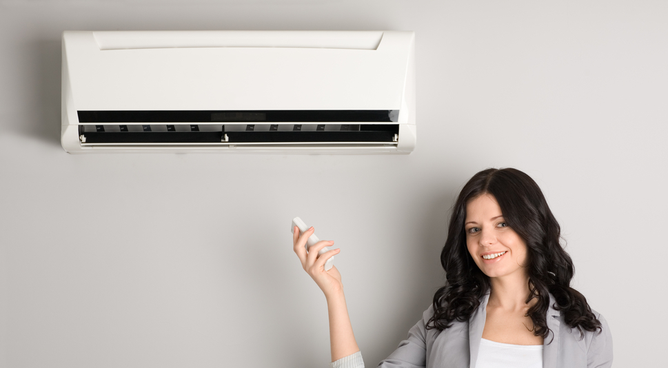A woman is holding a remote control in front of an air conditioner.