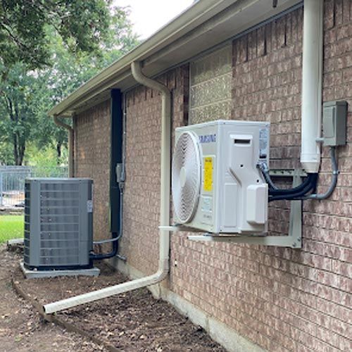 Two air conditioners are mounted on the side of a brick house.