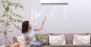 A woman is sitting on a couch in front of an air conditioner.