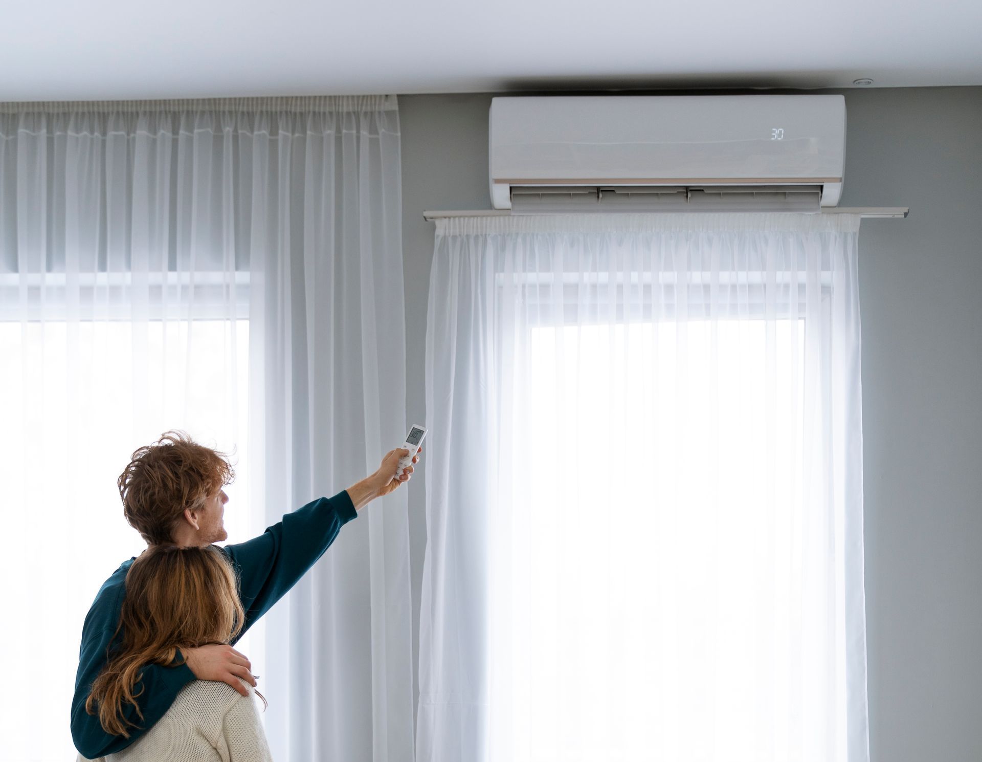 A man and a woman are adjusting the air conditioner in a living room.