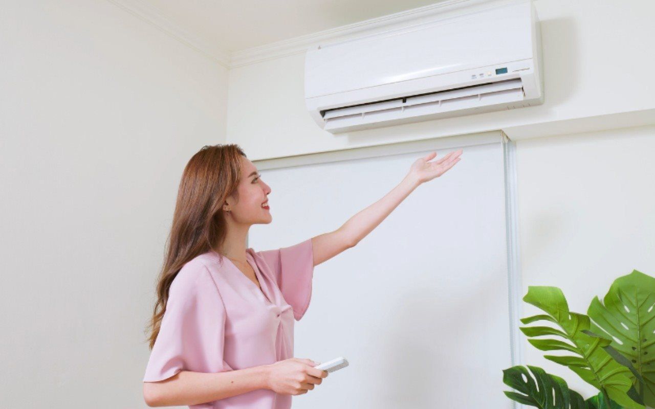 A woman is adjusting her air conditioner with a remote control.