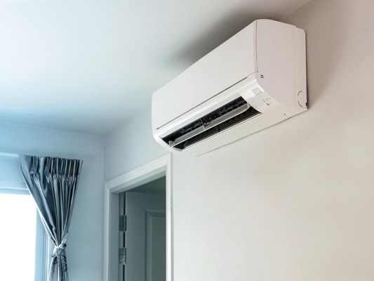 A white air conditioner is hanging on a white wall in a room.