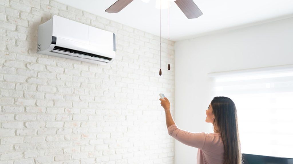 A woman is using a remote control to turn on an air conditioner in a living room.