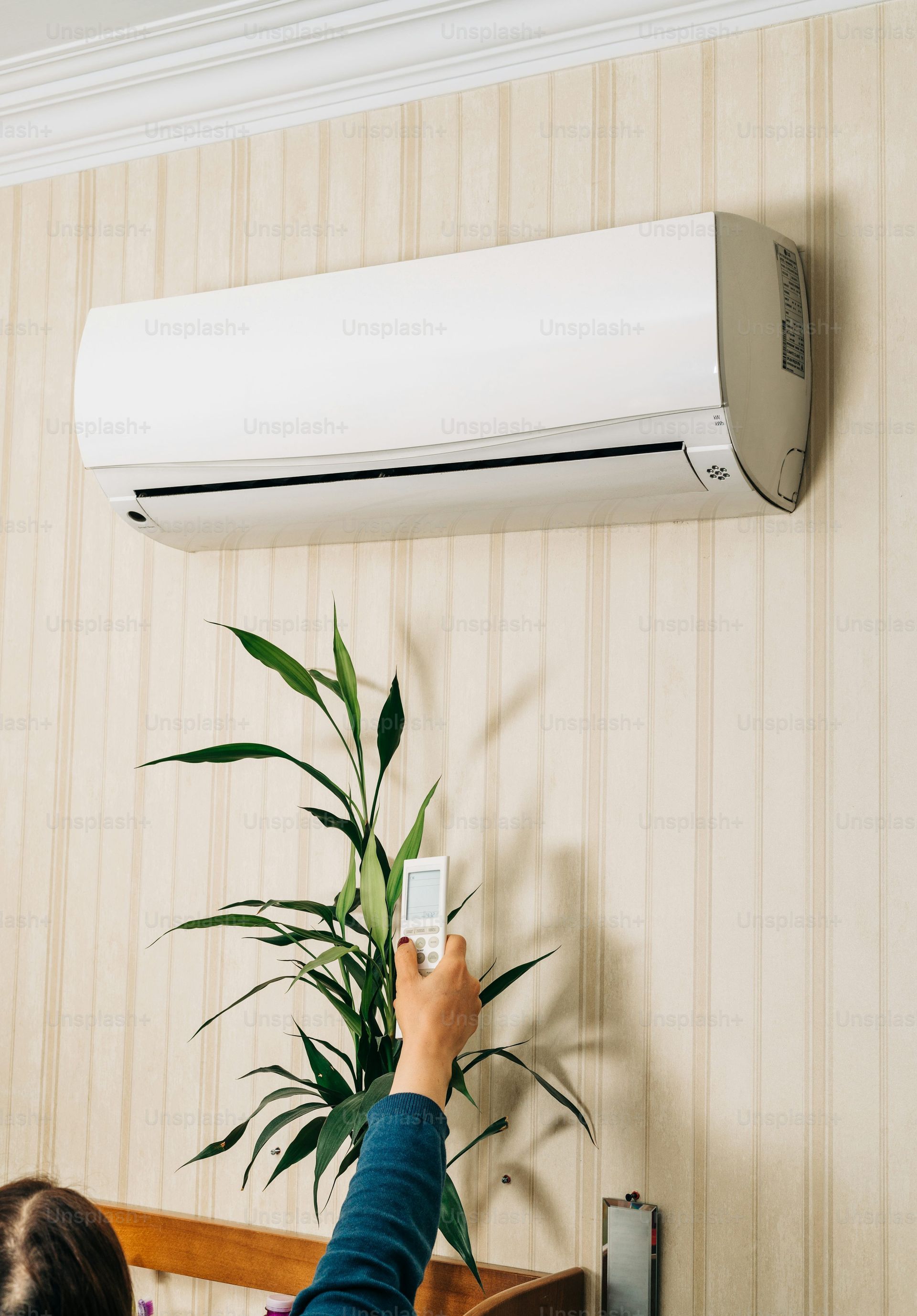 A person is holding a remote control in front of an air conditioner.