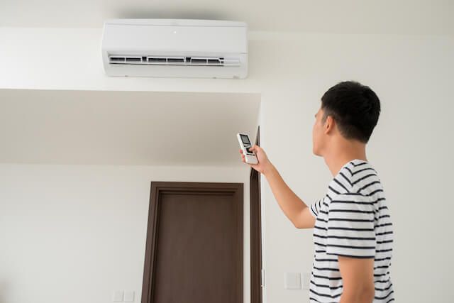 A man is holding a remote control in front of an air conditioner.