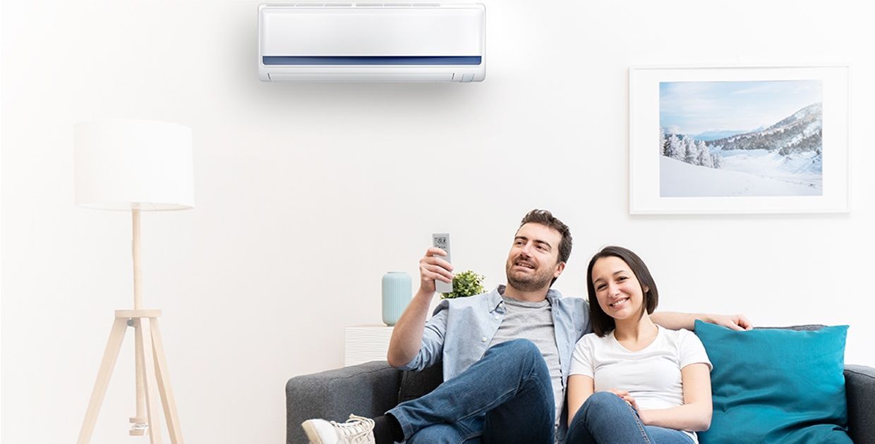 A man and a woman are sitting on a couch in front of an air conditioner.