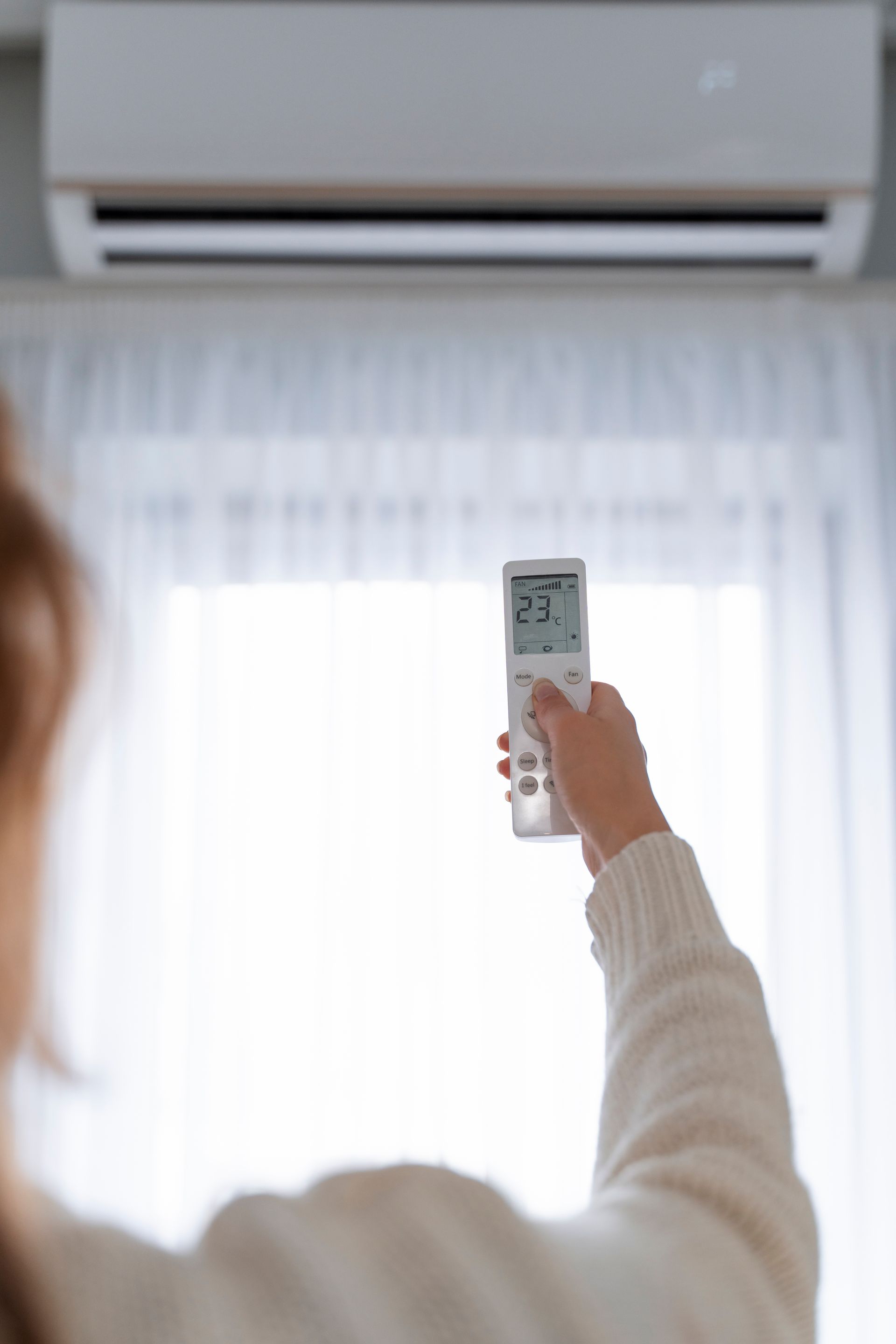 A woman is holding a remote control in front of an air conditioner.