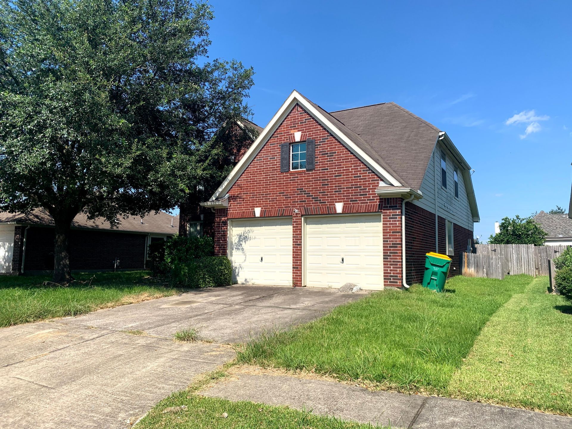 A house with two garage doors and a green trash can in front of it.