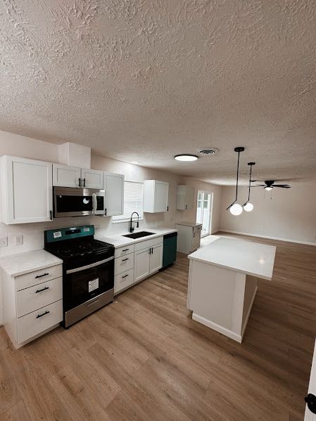 A kitchen with white cabinets , stainless steel appliances , a stove , sink , and microwave.