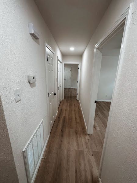 A long hallway with hardwood floors and white walls in a house.
