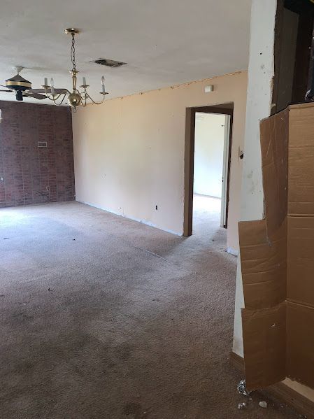 An empty living room with a ceiling fan and a brick wall.