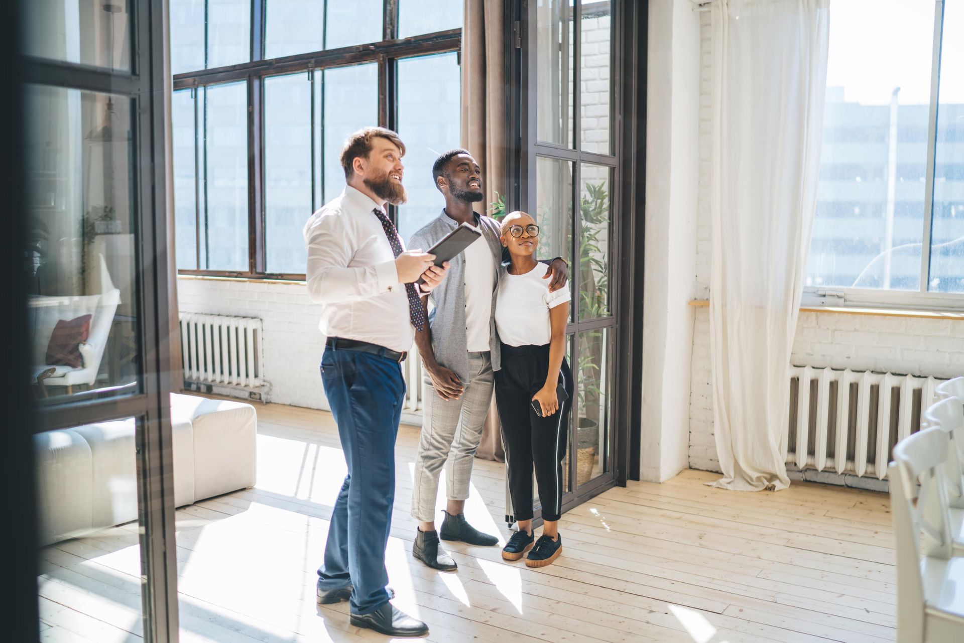 Real estate agent showing a couple a bright, open room with large windows.