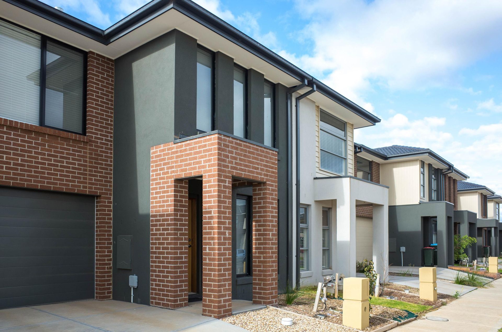 Modern townhouses with brick and gray facades, set against a blue sky.